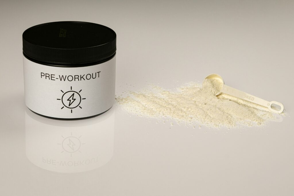 Pre-Workout-Pulver und Dosierlöffel auf einer reflektierenden Oberfläche, ideal zur Unterstützung beim Training und zur Vermeidung von Muskelabbau.