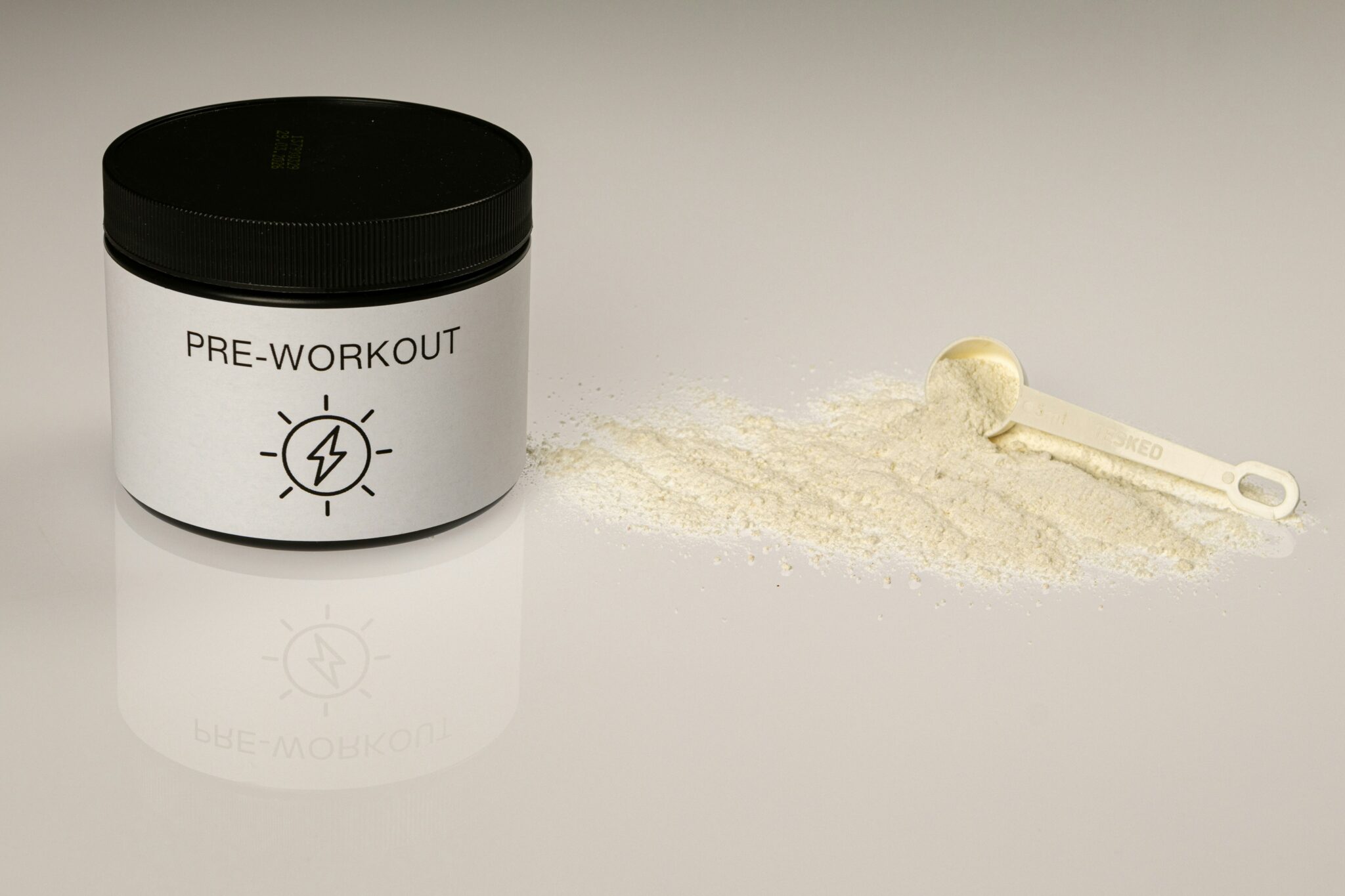 Pre-Workout-Pulver und Dosierlöffel auf einer reflektierenden Oberfläche, ideal zur Unterstützung beim Training und zur Vermeidung von Muskelabbau.