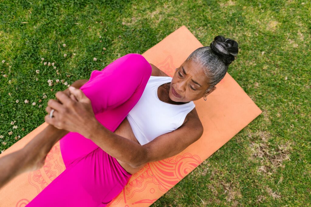 Ältere Frau macht Yoga-Dehnübung auf einer Matte im Freien, fördert Beweglichkeit und Gesundheit ab 40.