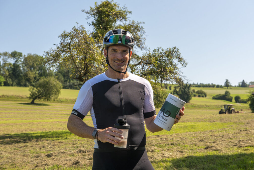 Ronnie Schildknecht, ehemaliger Triathlon-Spitzensportler, hält einen Proteinshake und eine Dose NoDoubt – Effizientes Training und Ernährung ab 40 für aktive Menschen.