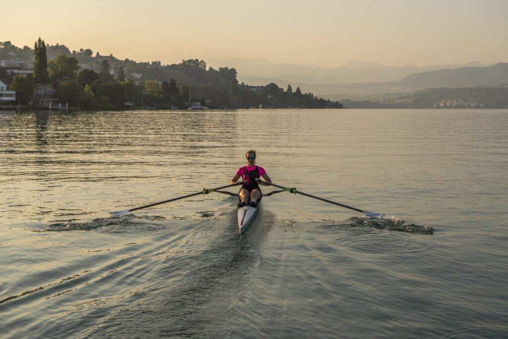 Ruderin im Einerboot bei Sonnenaufgang auf ruhigem See